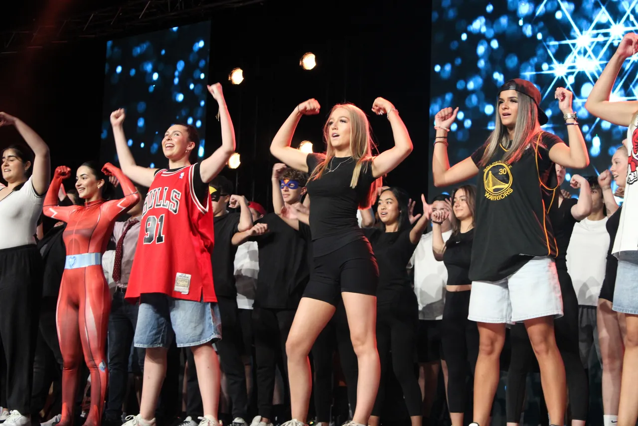A large group of upper secondary school aged students performing a synchronised dance number on stage, showcasing their talents as part of the much-loved annual Senior School House Performance.