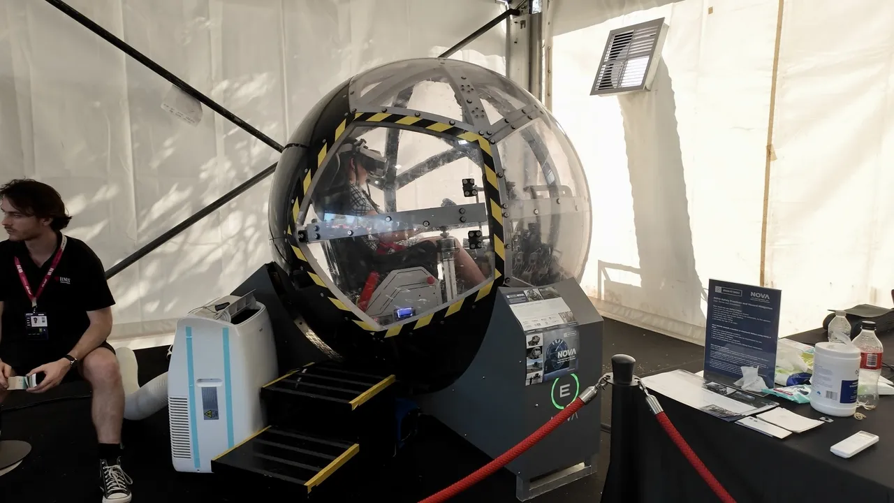 Overnewton upper secondary school aged VCE Vocational Major student seated inside a large spherical flight simulator, part of the interactive Driving Learning educational exhibit at the Melbourne Formula 1 Grand Prix.