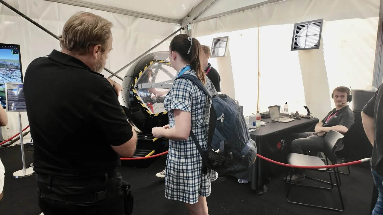 Overnewton upper secondary school aged VCE Vocational Major student engaged in a discussion with an exhibitor about a large spherical flight simulator, as part of the interactive Driving Learning educational exhibit at the Melbourne Formula 1 Grand Prix.