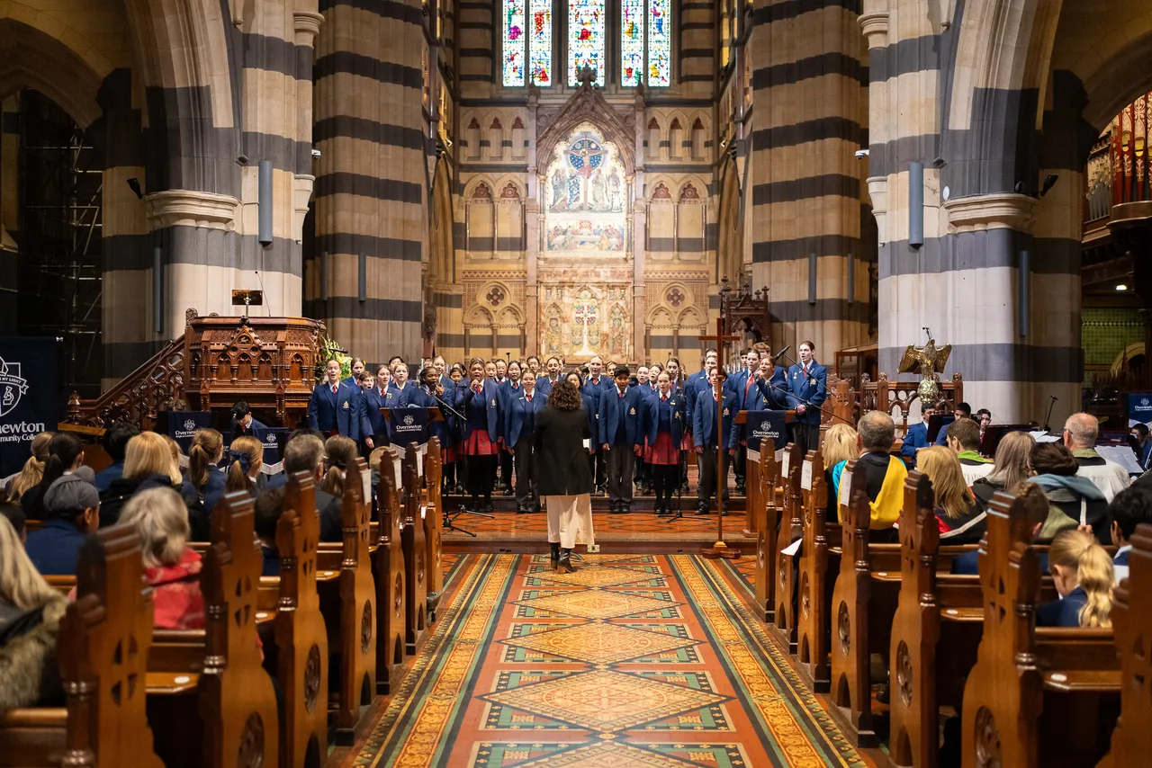 Wide angle shot of the interior of St Paul's Cathedral. Multiple rows of students and staff sit in pews watching a large choir on stage, singing as part of the Overnewton Anglican Community College 2025 Founders' Day Service.