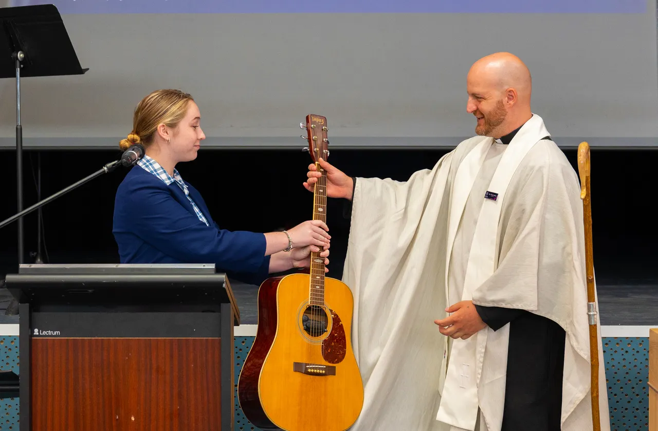 Reverend Peter being gifted a guitar by a student during his Commissioning Service at Overnewton, symbolising welcome, community, and the shared joy of music and ministry.