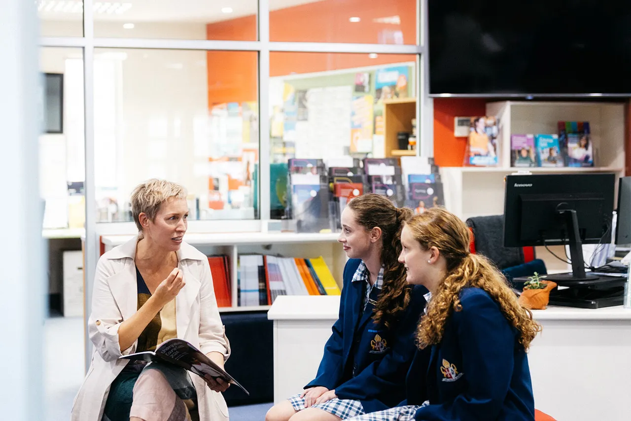 An engaged careers practitioner discussing university options with two senior secondary school aged students at Overnewton’s Careers Centre, holding a university course brochure.