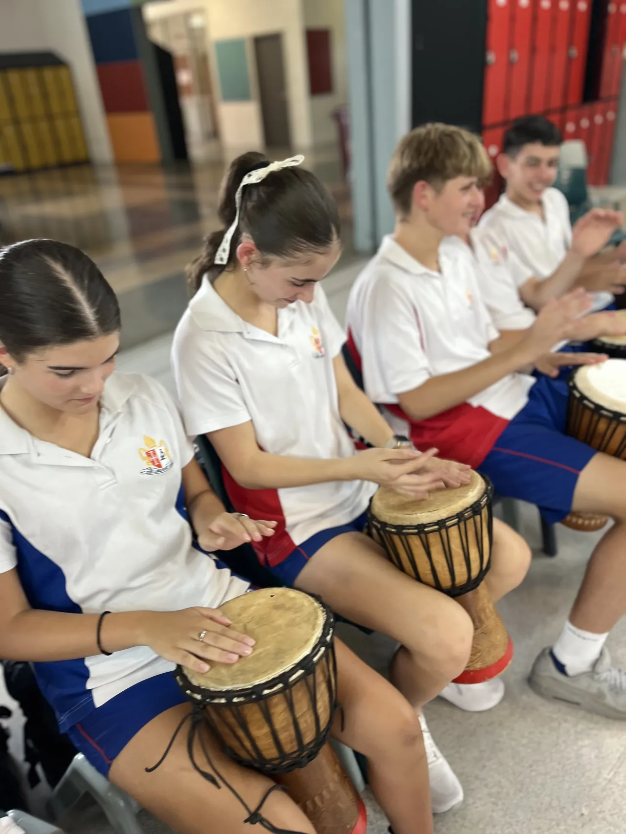Group of middle secondary school aged students fully engaged in an African drumming class, participating as part of a vibrant Year 9 House activity to kick off the school year.