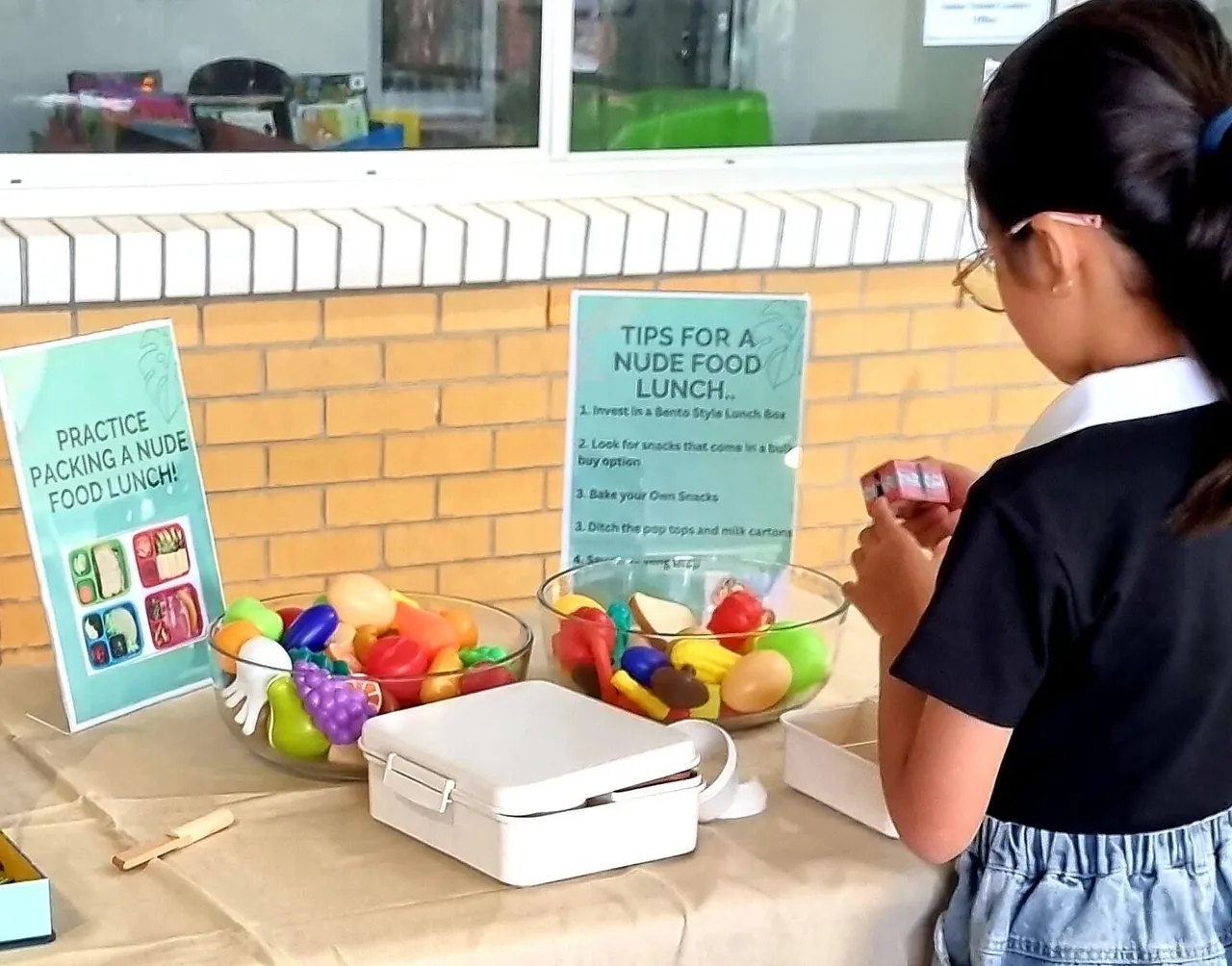 Lower primary school-aged child looking at display promoting healthy eating and Nude Food lunch boxes.