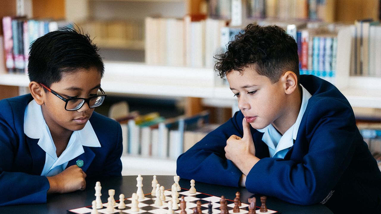 Two upper primary school aged students in the Middle School library at Yirramboi Campus, deep in thought while playing a game of chess together.