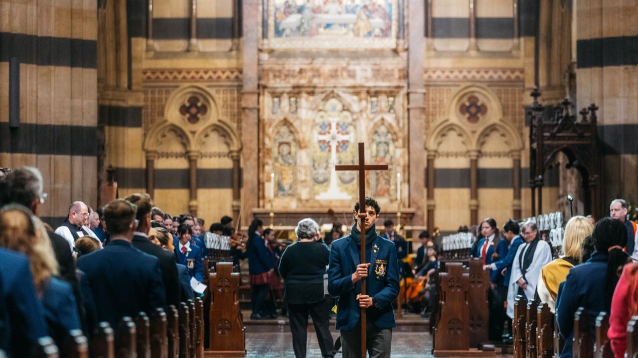 Student walking down the aisle at St Paul’s Cathedral carrying a cross during the Founders Day Service, representing Overnewton’s Anglican heritage and values.