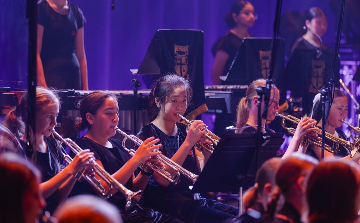 Secondary school girls performing in a brass ensemble at a Penrhos College music concert, playing trumpets on stage under professional theatre lighting.