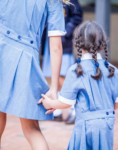 An older Ruyton student walking a younger Ruyton student from behind. They are both wearing summer uniform.