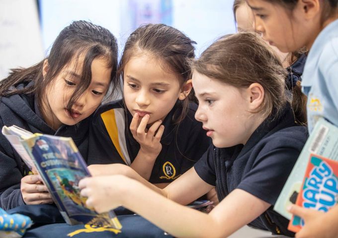 Three Ruyton students reading a book together in the Library