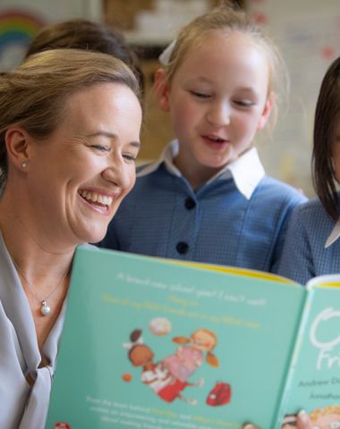 Teacher smiling while reading a picture book to junior school students.
