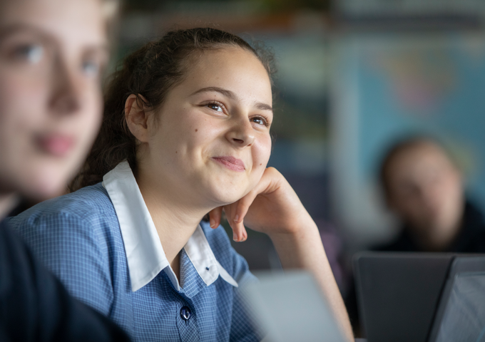 Student leaning on her hand, smiling up at the teacher in class.