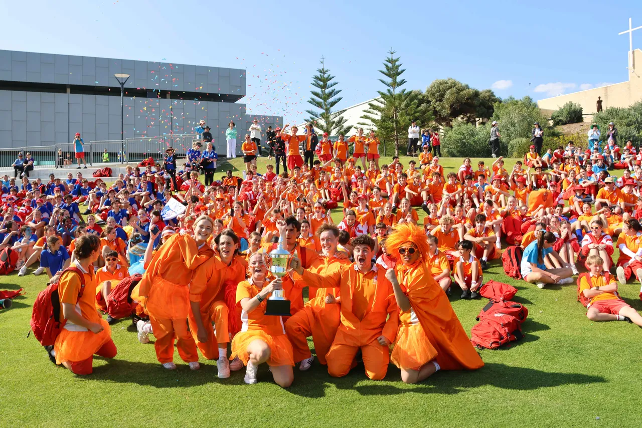 Students in Hannan (orange) celebrating a win with a trophy and confetti