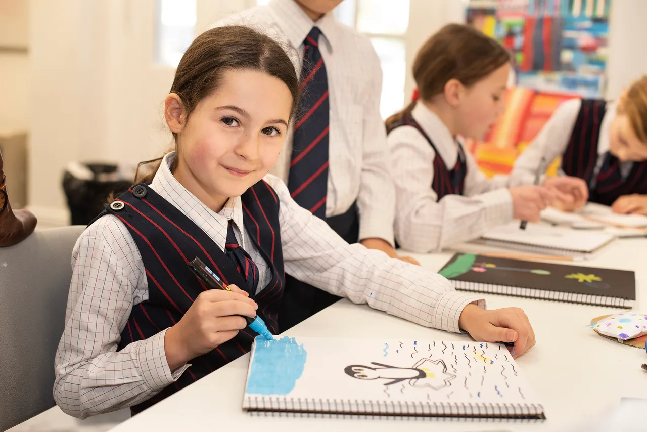 A St Michael's Grammar School primary student looks up from her artwork and smiles during a visual arts class, paintbrush in hand.