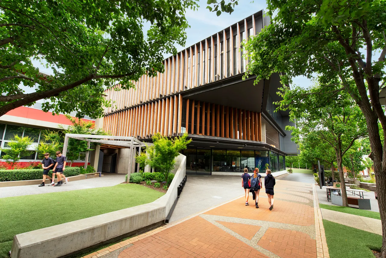 Photo of the Gipson Commons entrance lined with trees. Three students walk on the path towards the building.