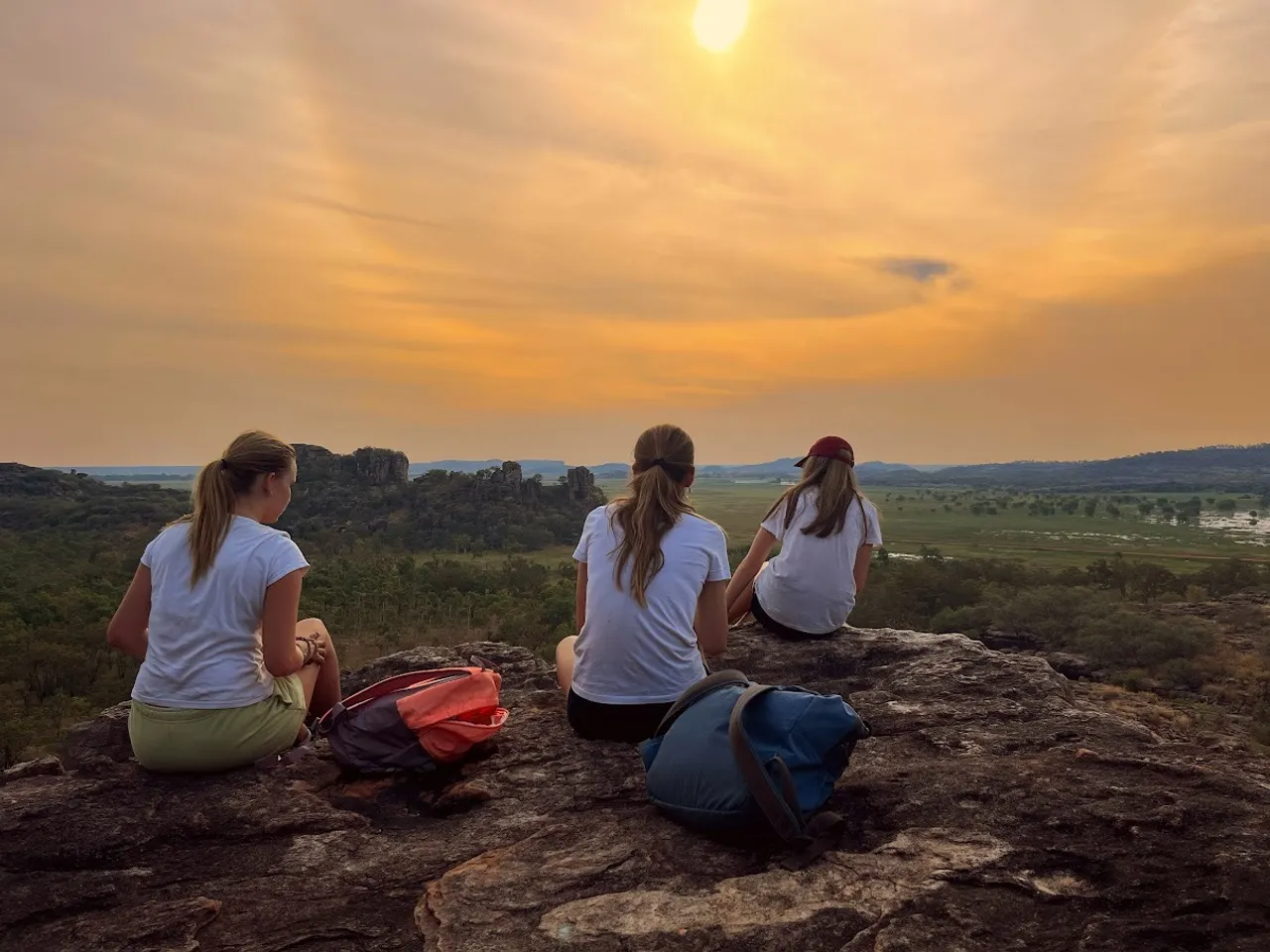 A group of St Michael's Grammar School students sit together on a rocky outcrop watching a sunset over a vast landscape, during an outdoor education expedition.