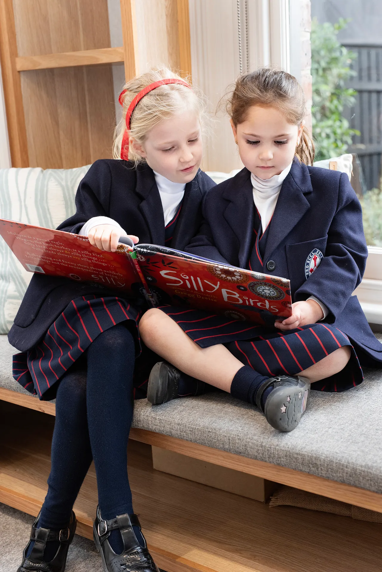 Two young St Michael's Grammar School students in winter uniform sit together on a bench, sharing a picture book.