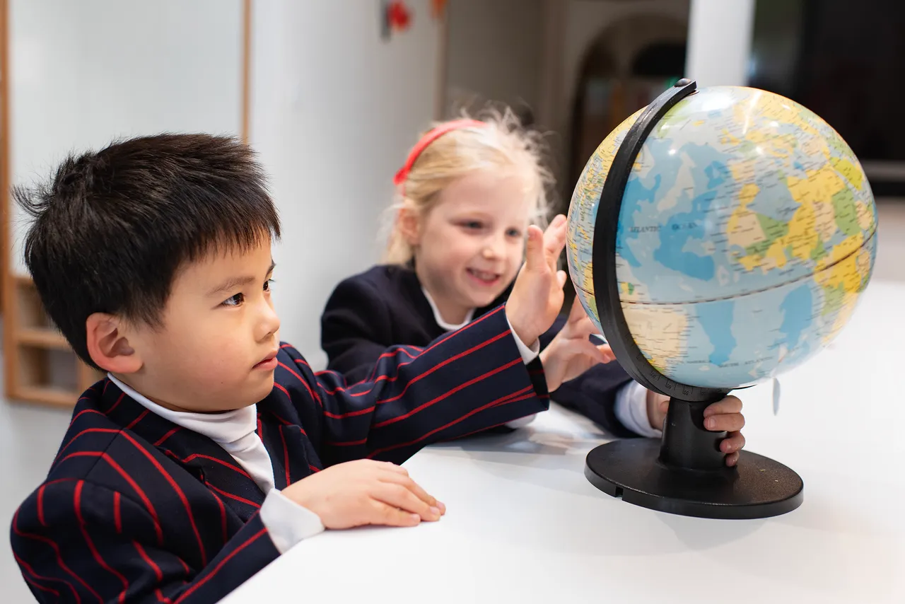 Two St Michael's Grammar School primary students lean in to explore a globe together during a classroom activity.
