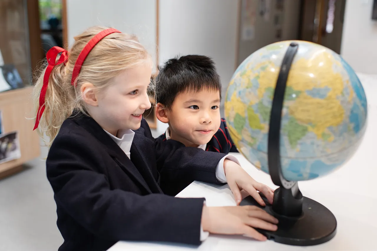 Two primary school students in St Michael's Grammar School uniform lean in together to examine a globe in the classroom.