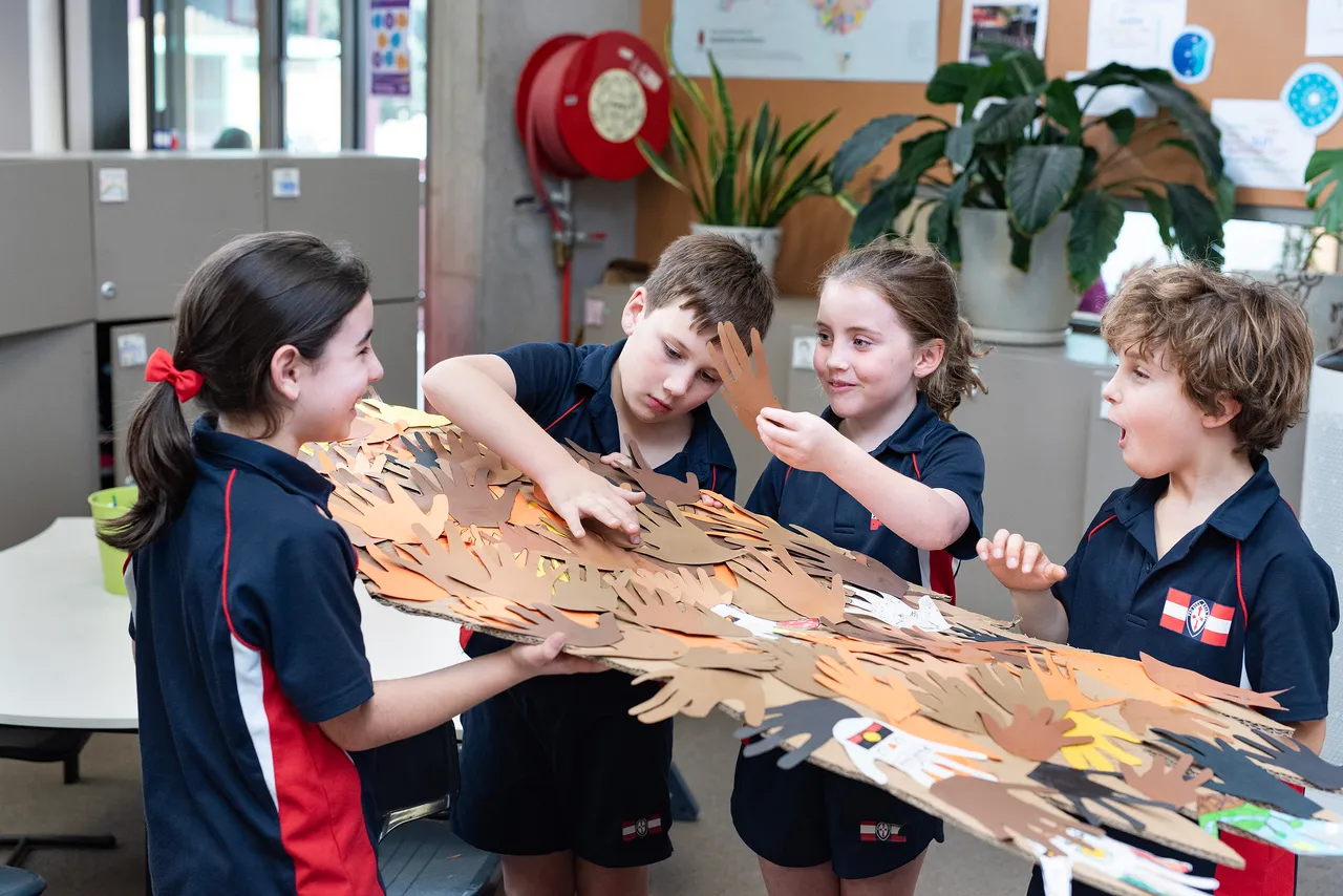 St Michael's Grammar School primary students collaborate on a large paper handprint artwork, likely as part of a cultural or community acknowledgement activity.