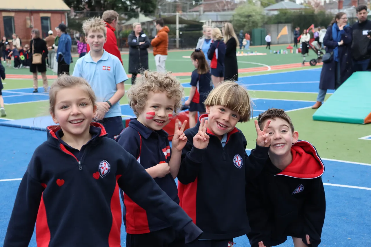 Four young St Michael's Grammar School students with face paint smile and pose for the camera on the school's sports courts during a school sports carnival.