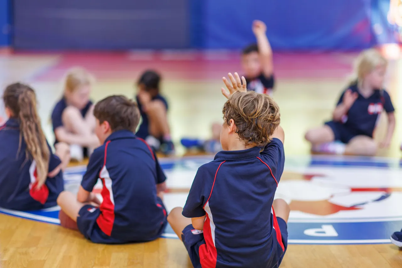Junior school students sitting in PE class on the floor of the St Michael's gymnasium.
