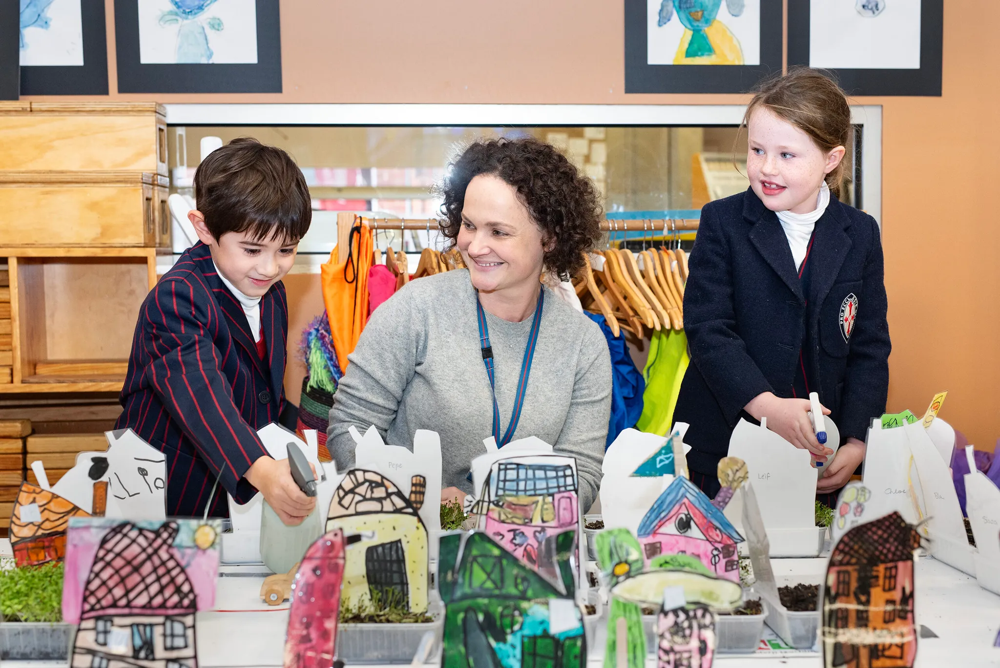 A St Michael's Grammar School teacher and two primary students examine handmade model buildings together during a creative arts class.