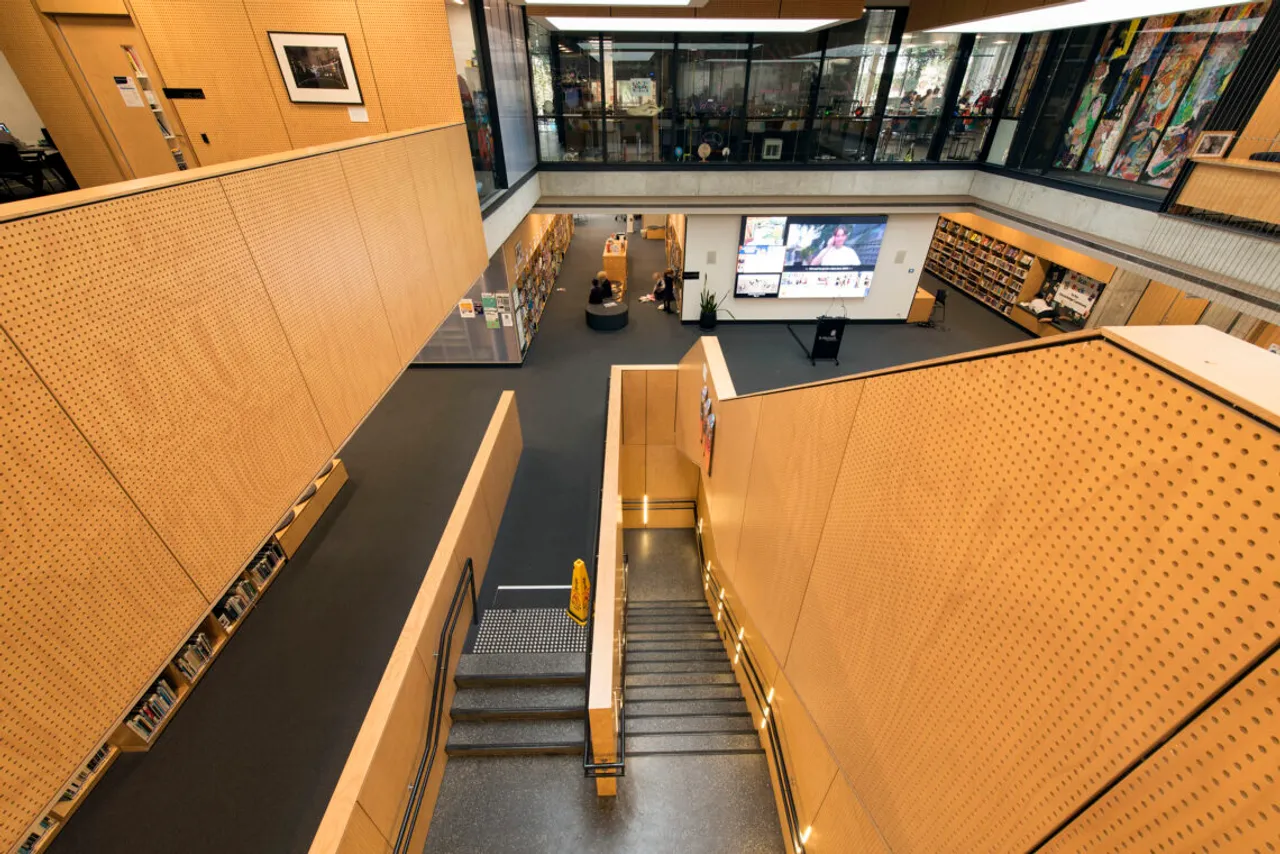 An overhead view of St Michael's Grammar School's library and learning centre, showing bookshelves, a large digital display screen and a central staircase.