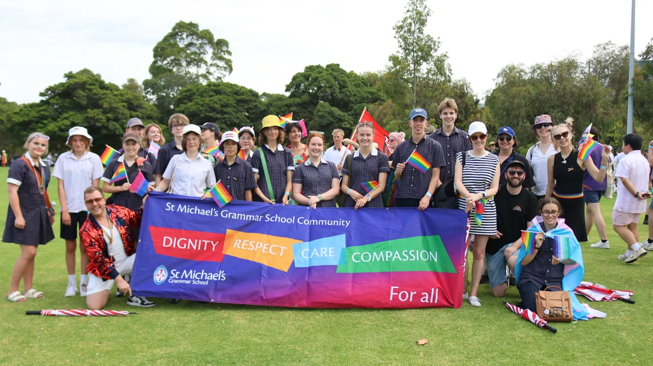 St Michael's community members, students and staff hold up a school community banner with the school's values of Dignity, Respect, Care and Compassion