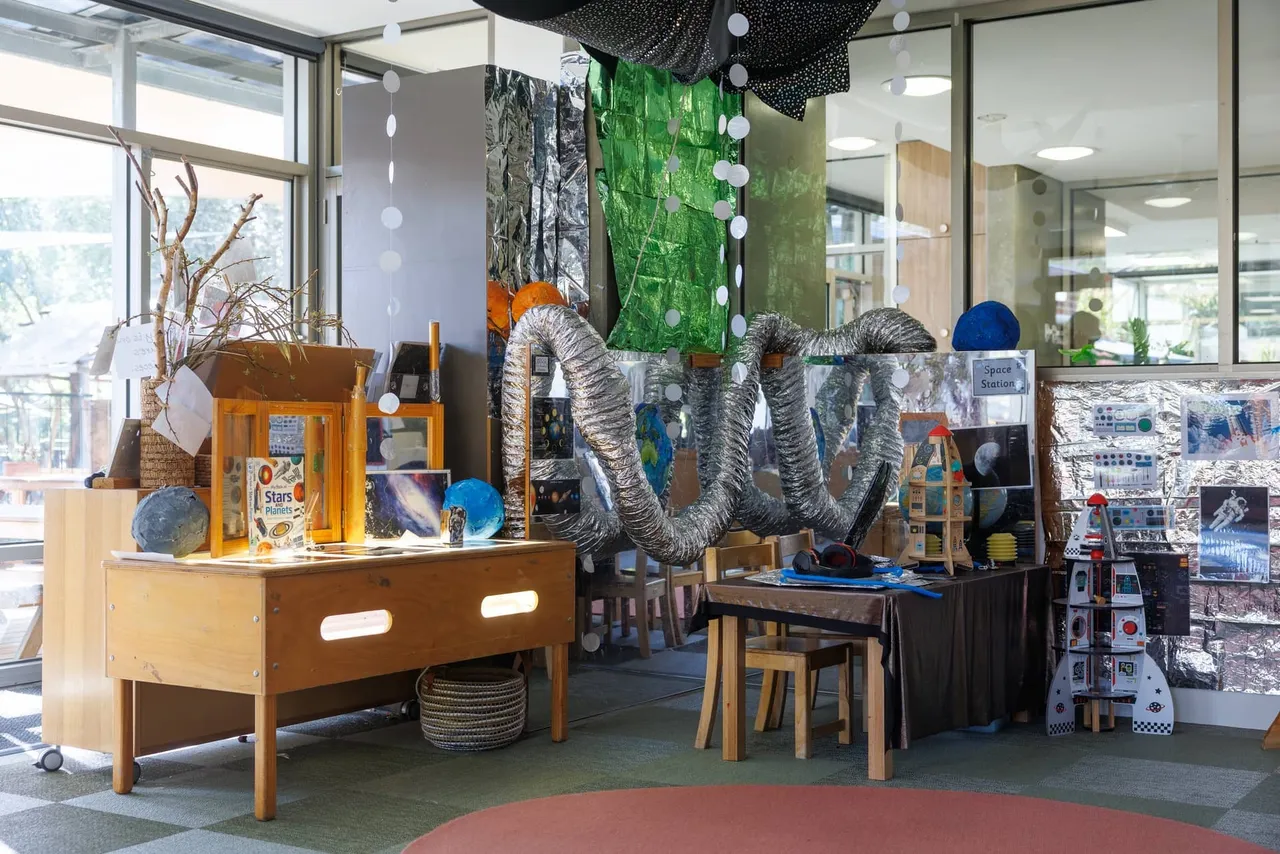 A richly decorated space-themed learning environment in the St Michael's Grammar School ELC, featuring a light table, planet models, a cardboard rocket and imaginative loose materials for exploration.