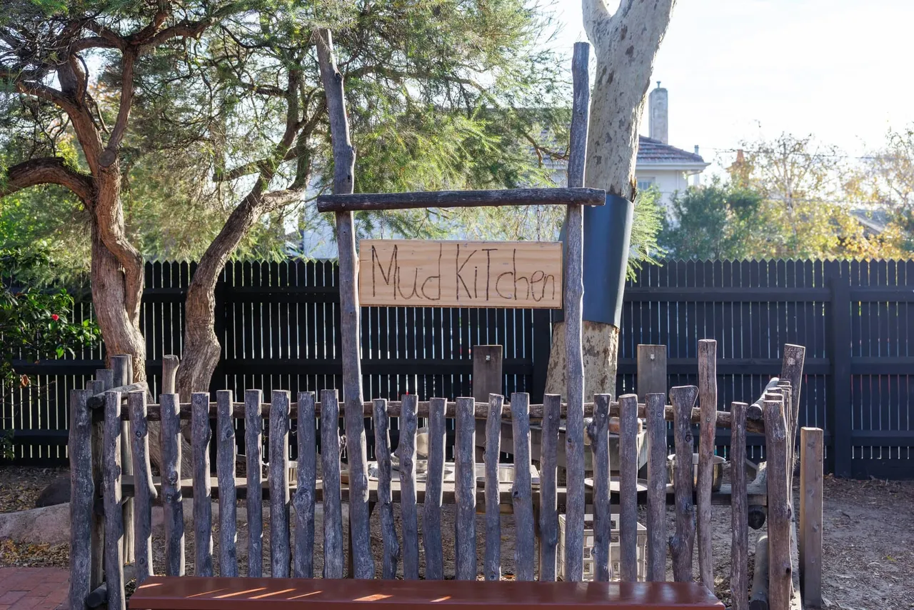The mud kitchen in the St Michael's Grammar School ELC outdoor play area, framed by natural timber fencing and established trees.