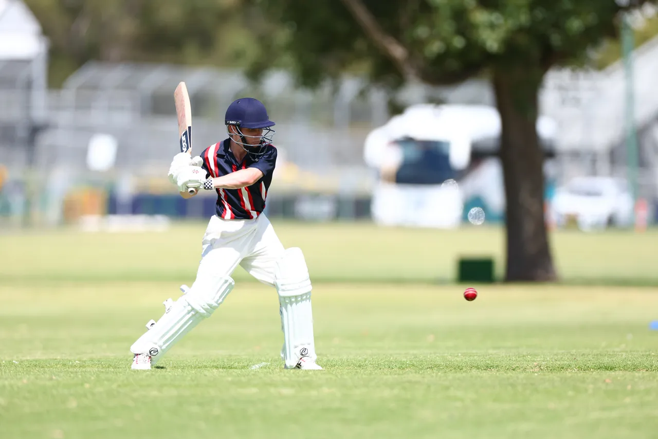 A St Michael's Grammar School student in full batting gear plays a shot during an outdoor cricket match.