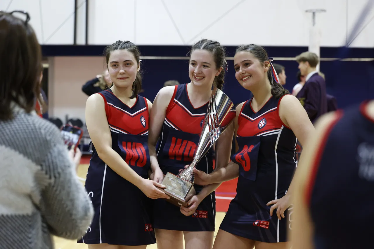 Girls netball team celebrate win with first place trophy.