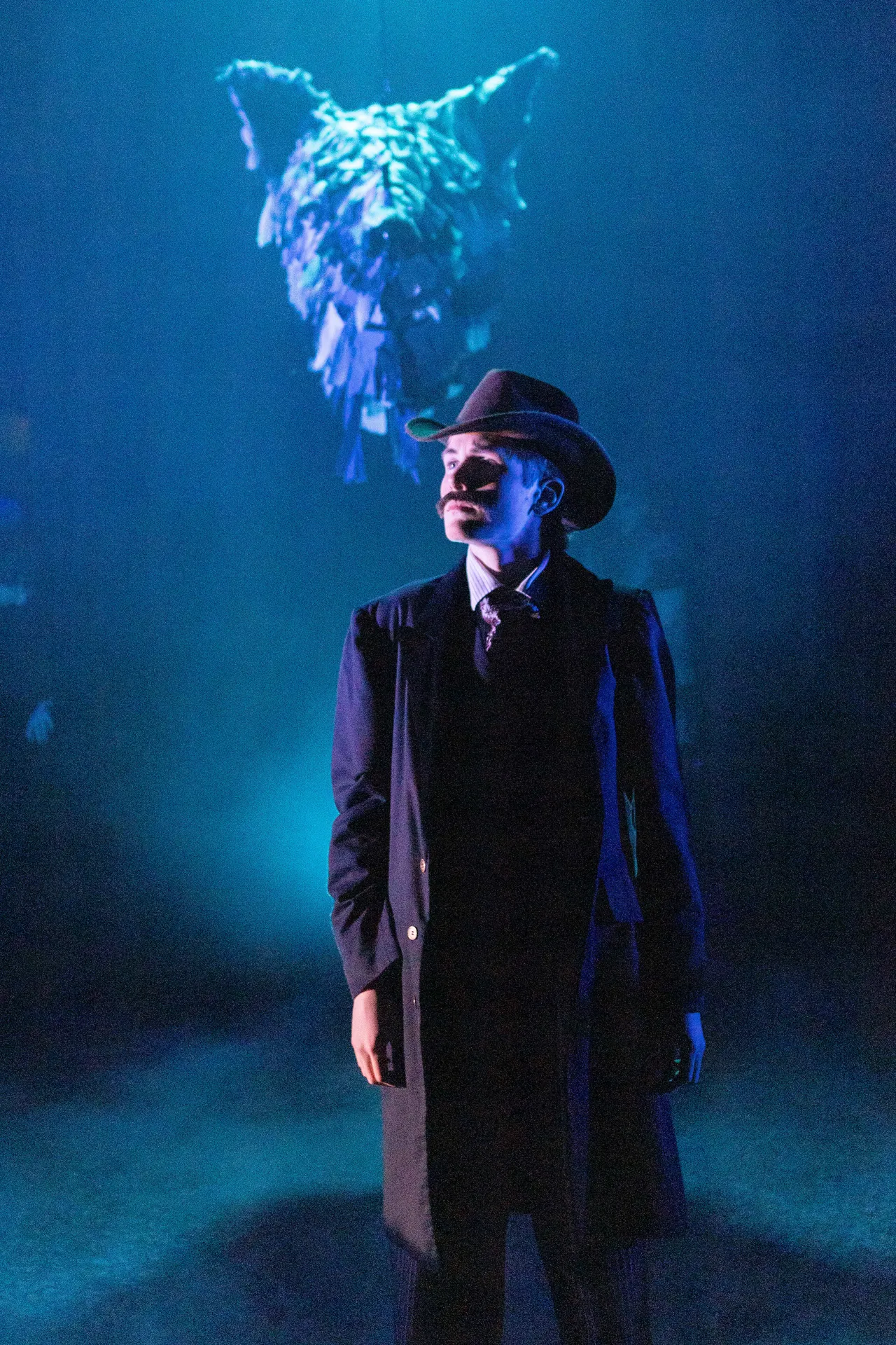 A St Michael's Grammar School student in full costume and stage makeup performs under dramatic blue lighting during a school theatrical production.