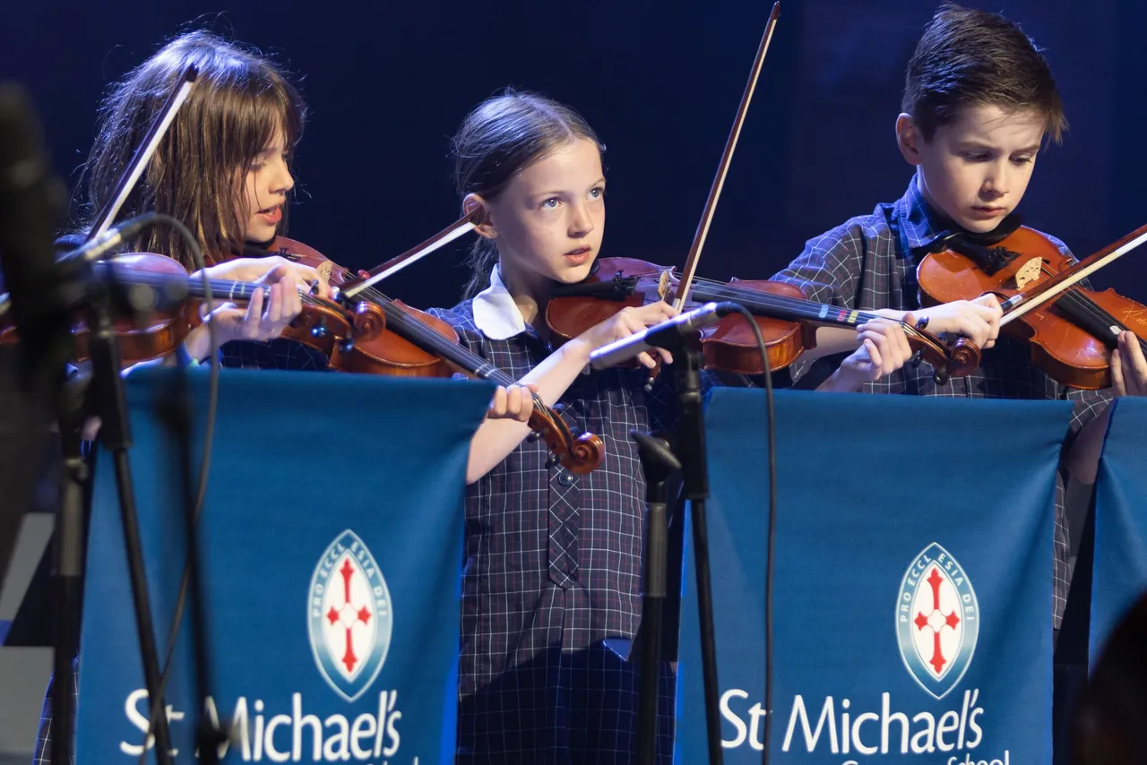 Students perform on stage playing the violin during a School address