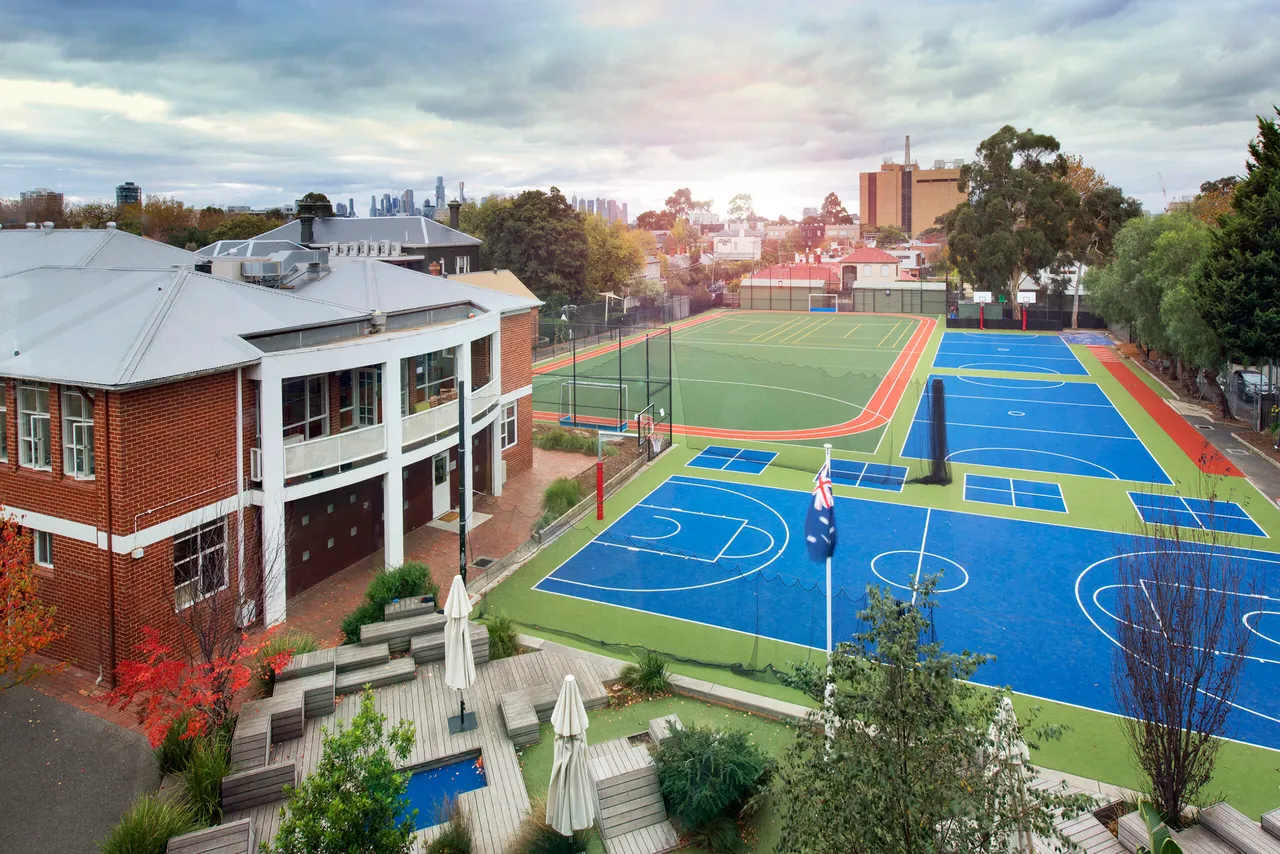 An aerial view of St Michael's Grammar School's campus showing the school building alongside its outdoor sports courts, with the Melbourne city skyline visible in the background.