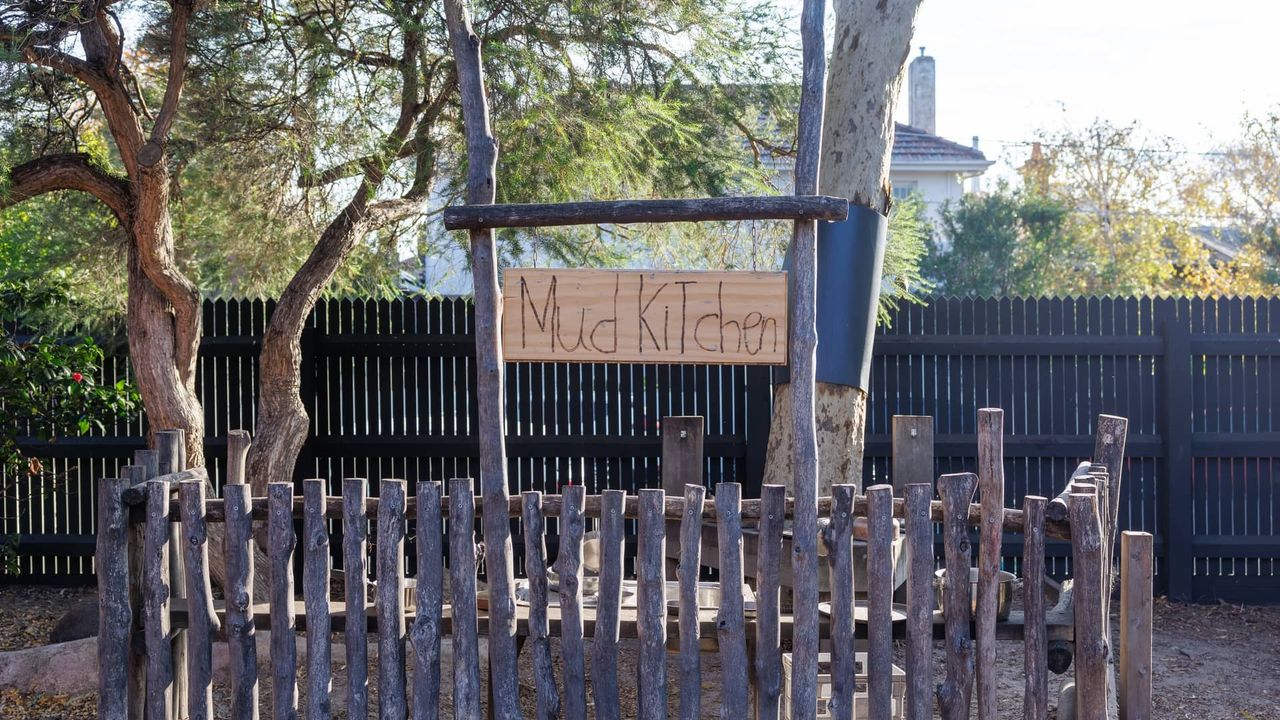 The mud kitchen in the St Michael's Grammar School ELC outdoor play area, framed by natural timber fencing and established trees.