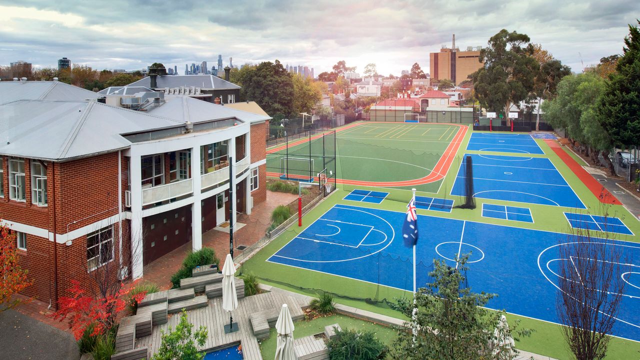 An aerial view of St Michael's Grammar School's campus showing the school building alongside its outdoor sports courts, with the Melbourne city skyline visible in the background.